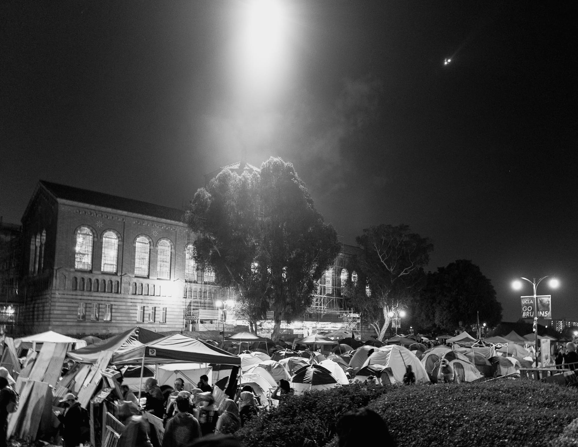 A helicopter shines its light on an encampment at UCLA.