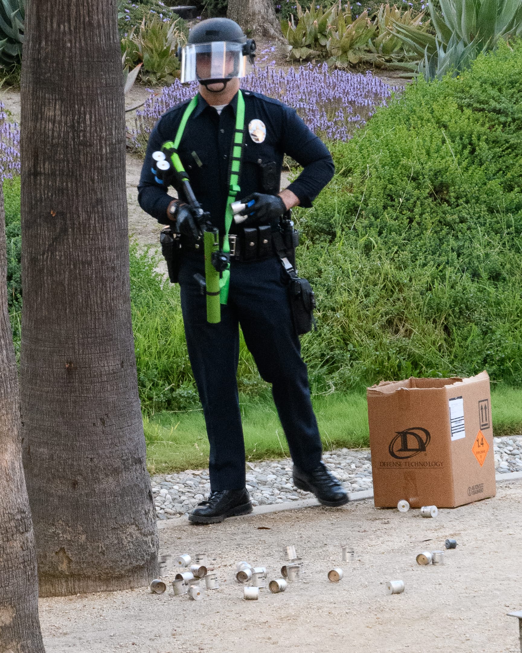 An LAPD officer armed with a less lethal launcher stands next to a box of 40mm foam rounds