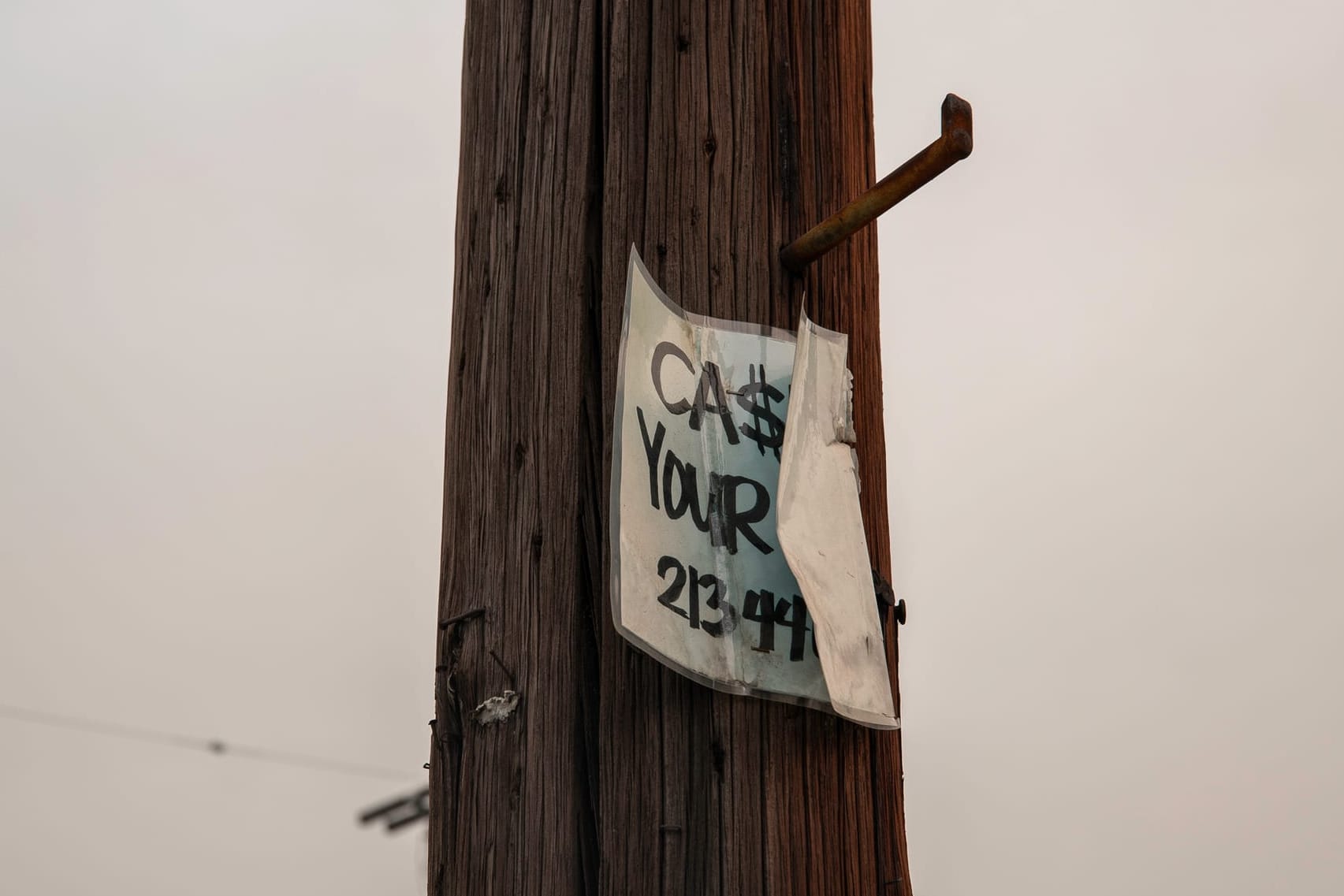 A power pole with a bent sign stapled to it. 