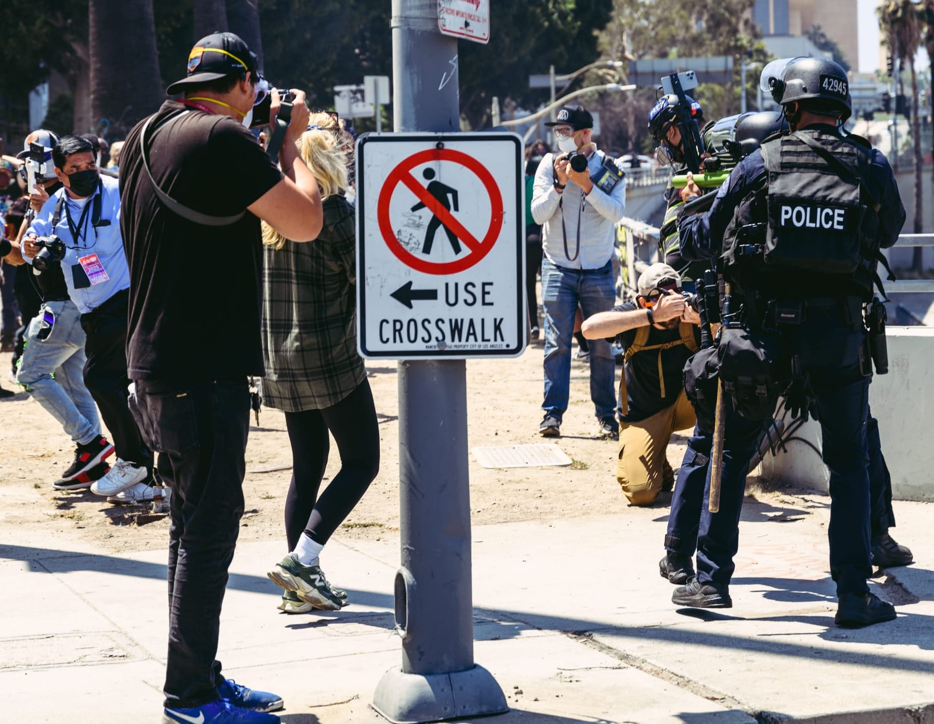 People, including journalists, flee as police officers in riot gear point guns at them.