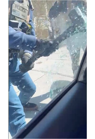 A police officer smashes the window of a car with a metal pick to remove an undocumented person from their car. 